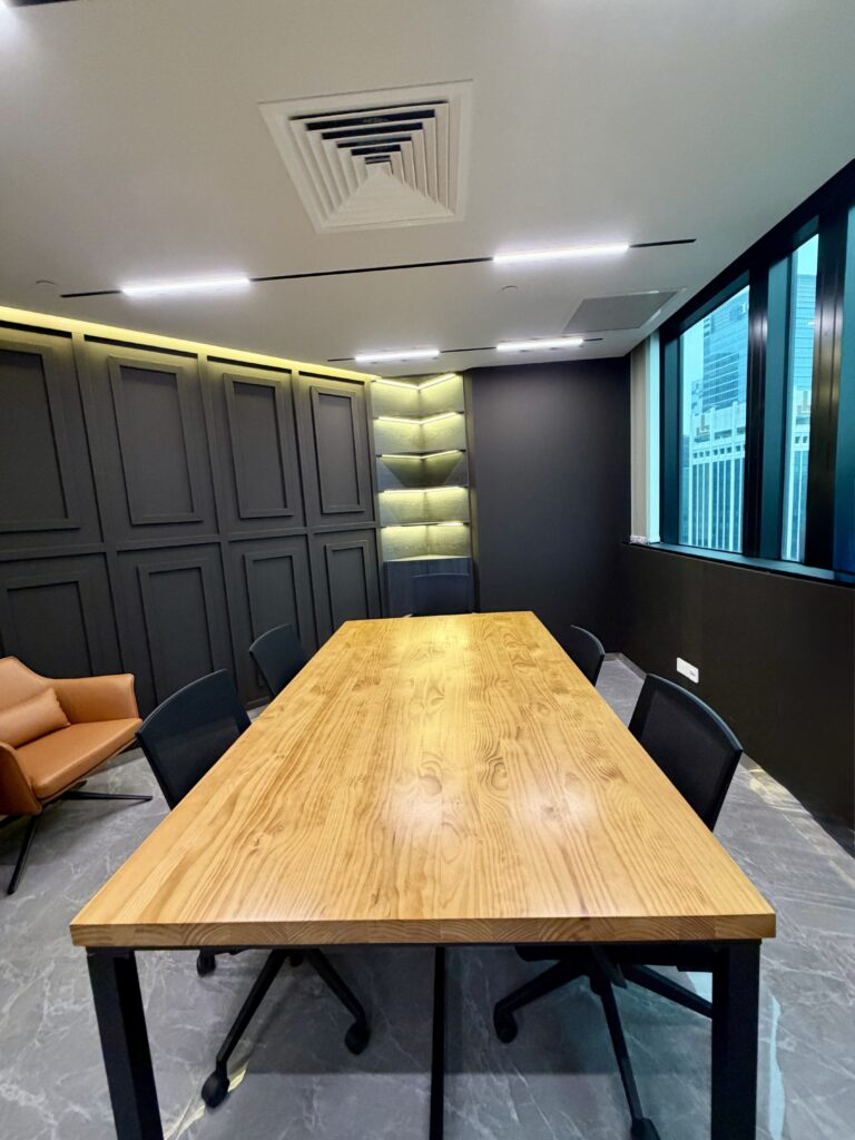 Conference room with a long wooden table, four black chairs, and an orange armchair against panelled walls.
