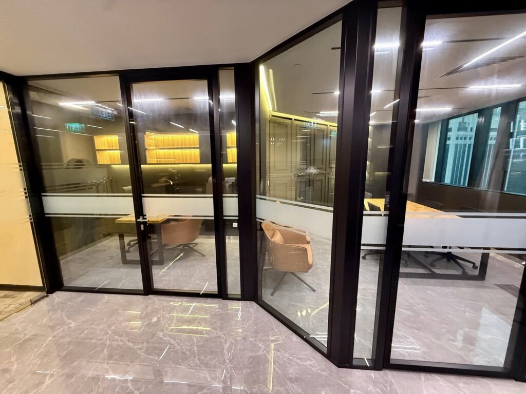 Glass-walled office cubicles with brown armchairs, desks, and marble flooring.