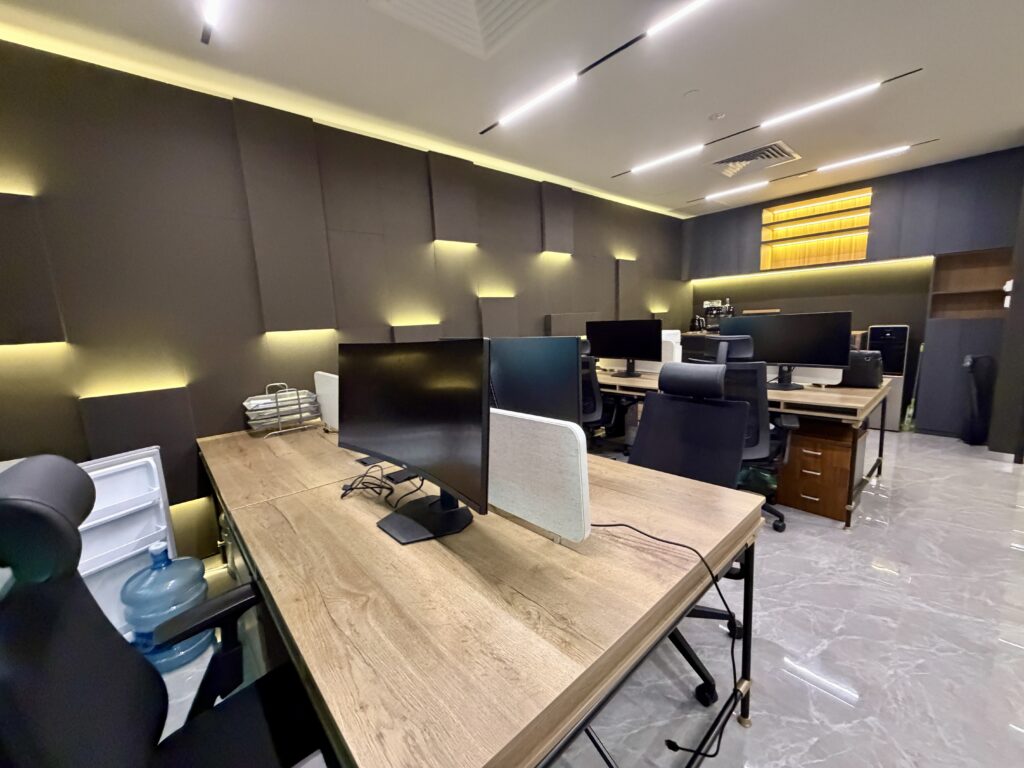 Modern office space with wooden desks, black task chairs, and computer monitors.