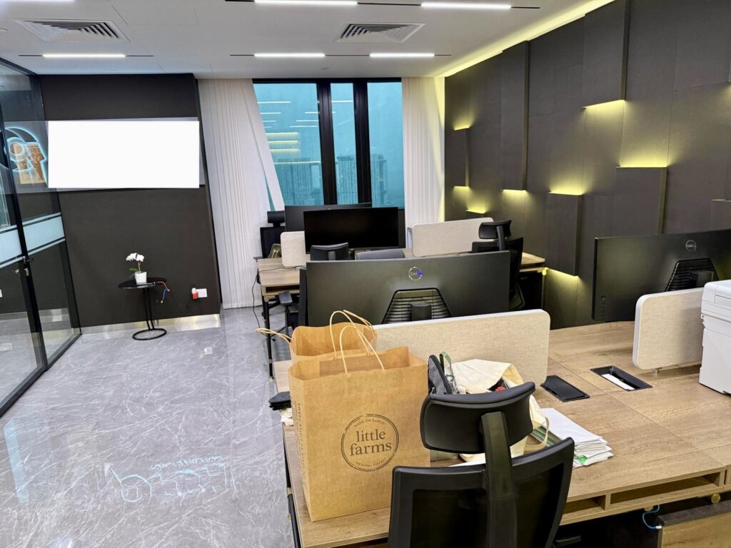 Modern office space with desks, computer monitors, and a Little Farms paper shopping bag in the foreground.