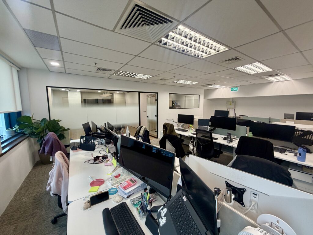 An open-plan office space with rows of white desks, computer monitors, and chairs.