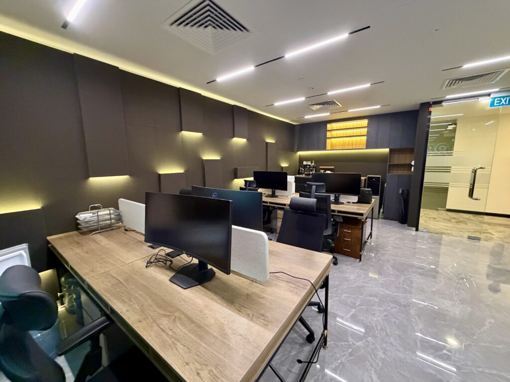 Office space with rows of wooden desks, computer monitors, and black office chairs.