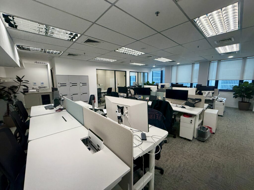 Rows of white office desks with computer monitors and chairs in an open-plan workspace.