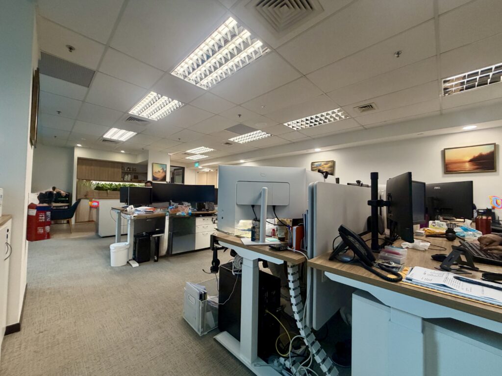 A view of an open-plan office space featuring several desks with computer monitors and office equipment.