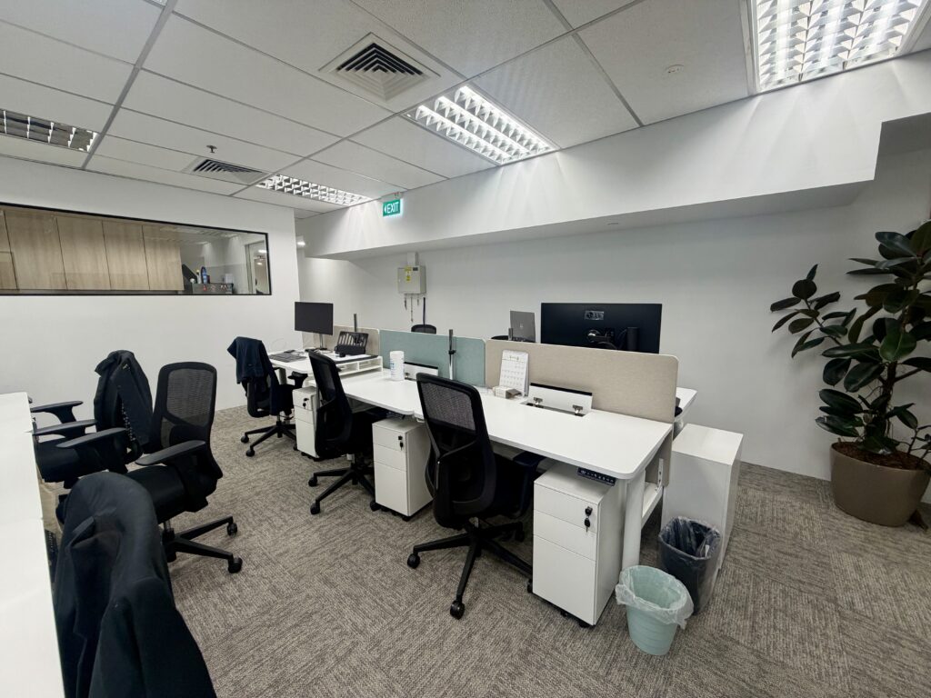 Office interior with rows of white desks, black swivel chairs, and computer monitors.