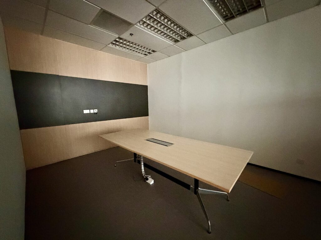 An empty meeting room with a large wooden conference table and a wall with a dark horizontal panel.