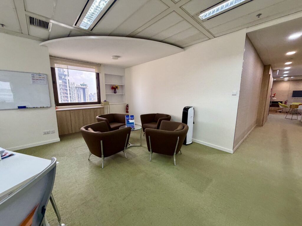 Four brown armchairs arranged around a small glass table in an office meeting area.