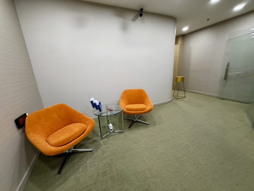 Two orange swivel chairs separated by a small glass side table in a waiting area.