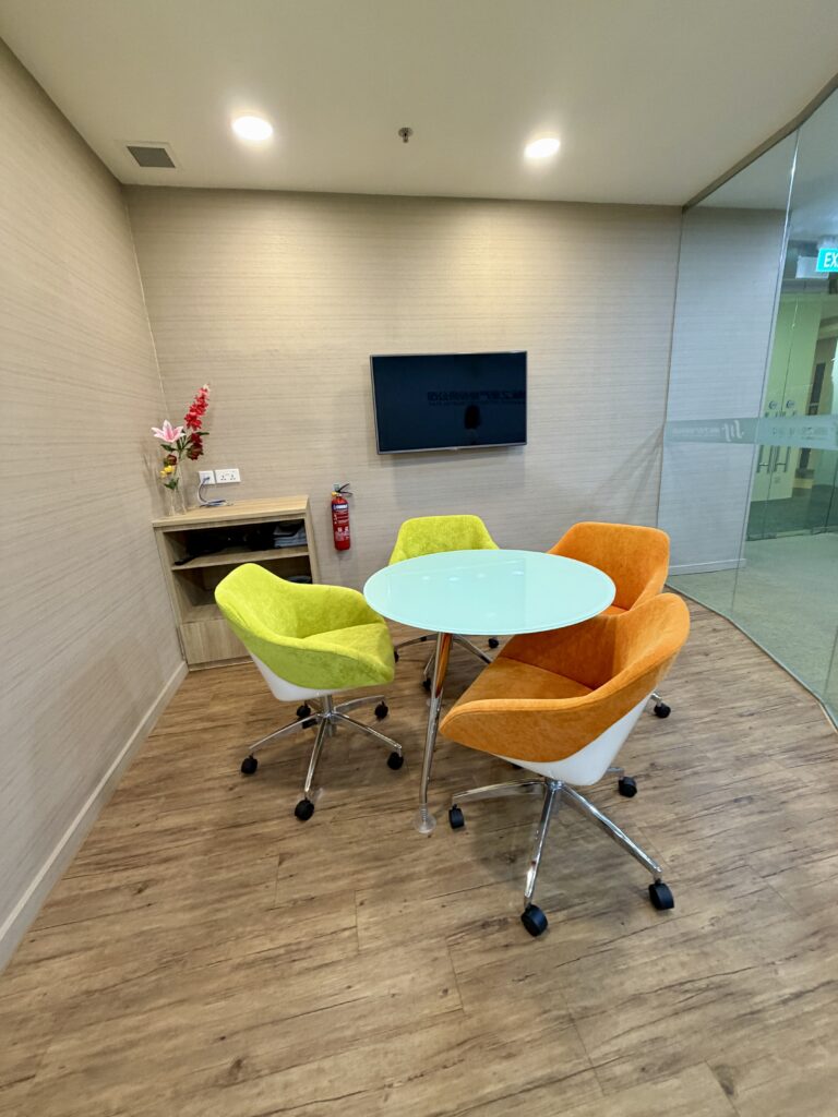 A small round table with two lime green and two orange swivel chairs in a meeting area.