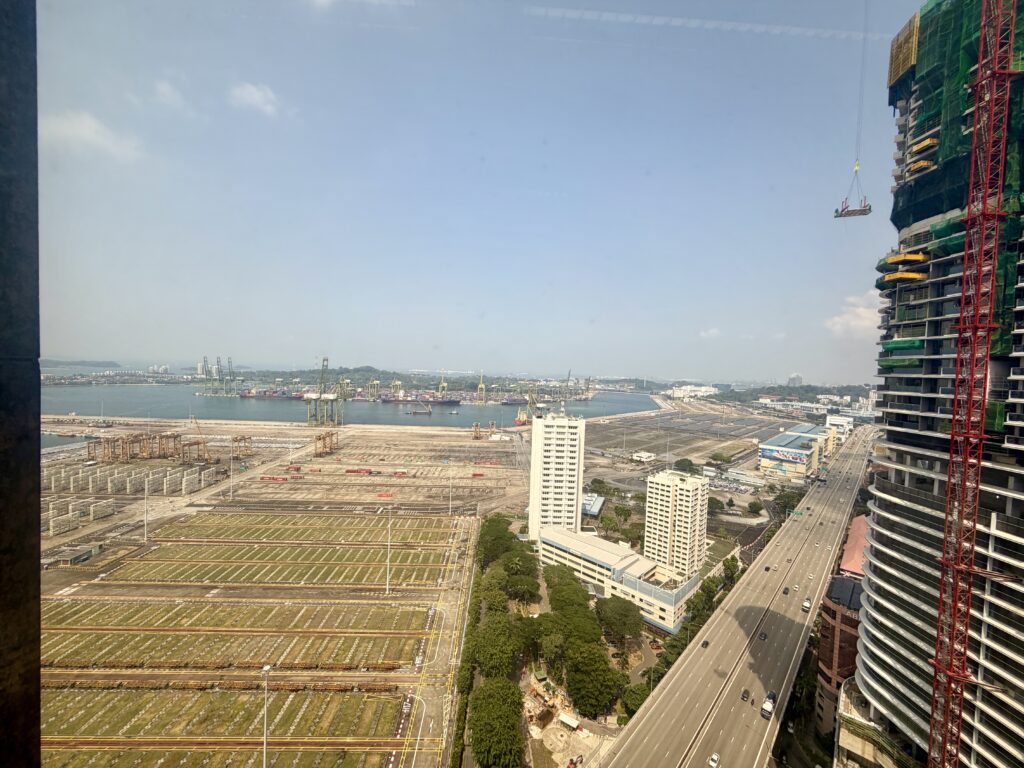 High-angle view of a shipping port, a motorway, and a tall building under construction with a suspended work platform.