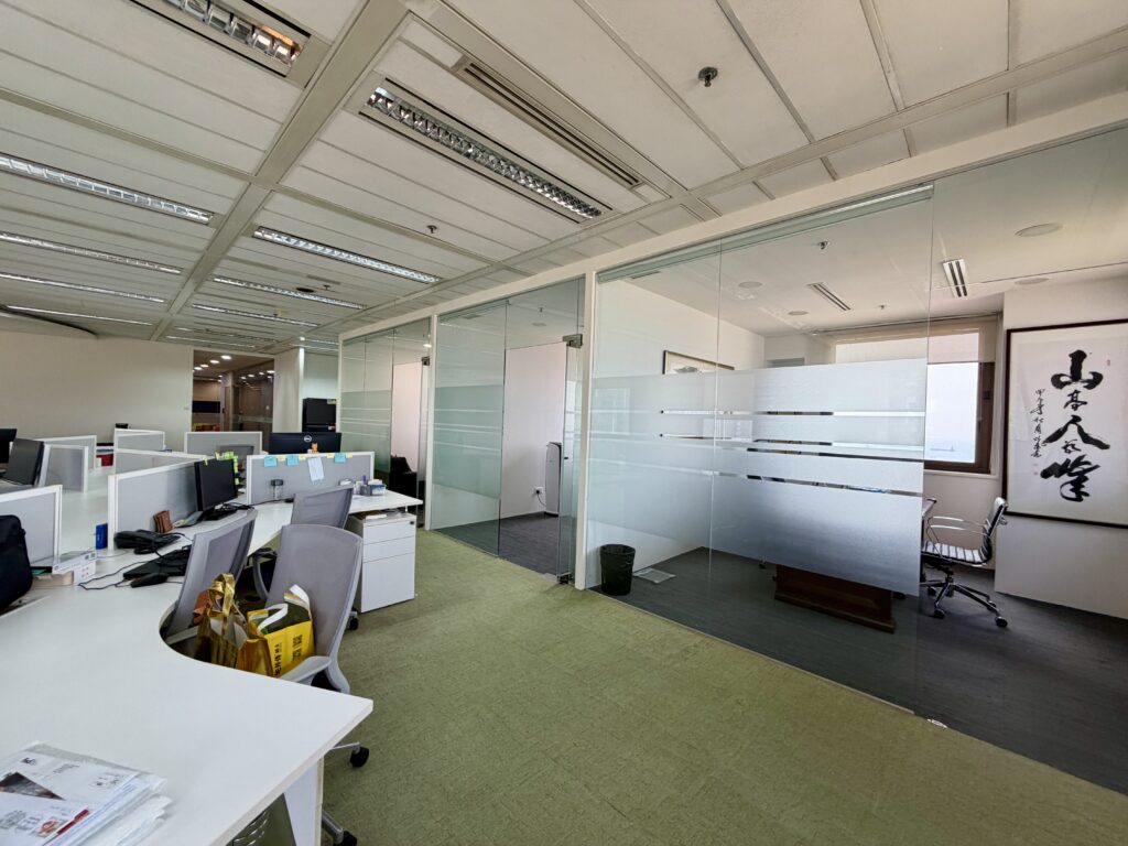 Office interior featuring open workstations in the foreground and glass-walled meeting rooms in the background.