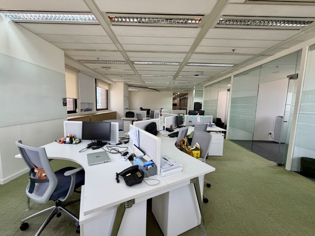Empty office space with white curved desks, office chairs, and glass partition walls.