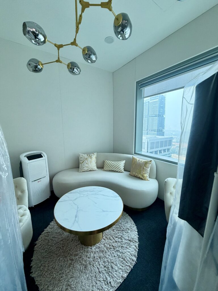 A lounge area with a curved white sofa, marble-topped coffee table, and air purifier, set against a window overlooking city buildings.