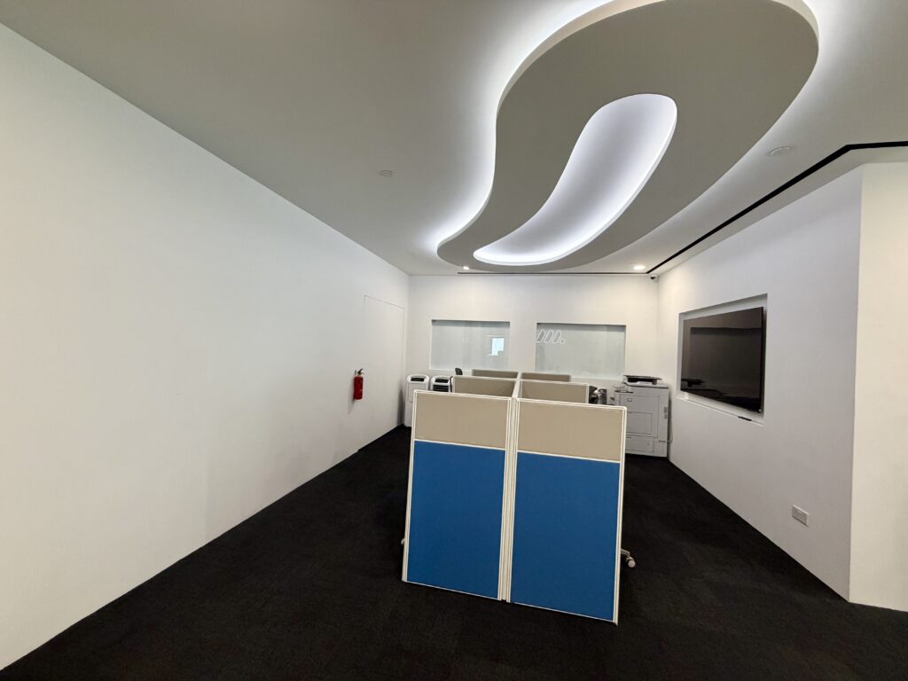 Modern office area featuring blue and beige cubicle partitions under an abstract ceiling light fitting.
